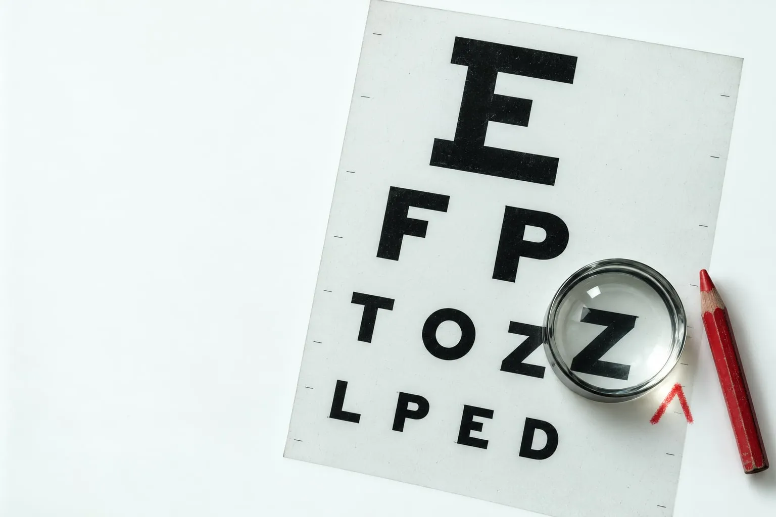 An eye-chart film on a lightbox, a loupe resting on the letter Z, next to a red pencil and a red caret.